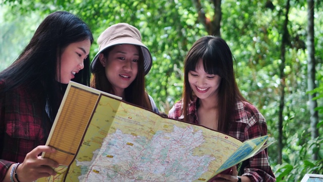 一群朋友十几岁的亚洲女性在森林里互相帮助找到旅行方向地图视图。冒险假期。视频素材