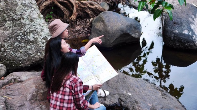 一群朋友十几岁的亚洲女性在森林里互相帮助找到旅行方向地图视图。冒险假期。视频素材