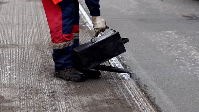 道路维修。工作细节上，工人们将树脂浇筑路面以覆盖沥青。视频素材