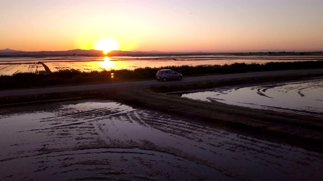 夕阳西下，一辆汽车低空飞过淹水的稻田视频素材