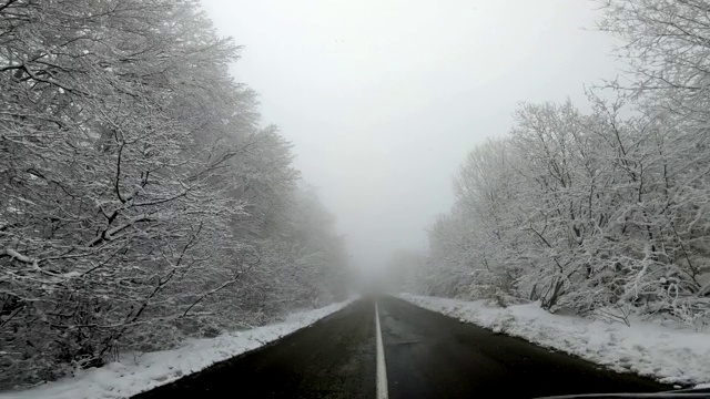 在冬季大雾天气下行驶在乡村的山路上，路上的树木被雪覆盖视频素材