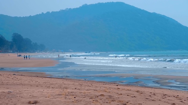 大浪在海滩上翻滚，远处一座山上长满了棕榈树视频素材