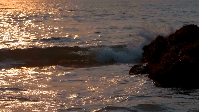 太阳反射在海面上，海浪拍打着海岸的岩石视频素材