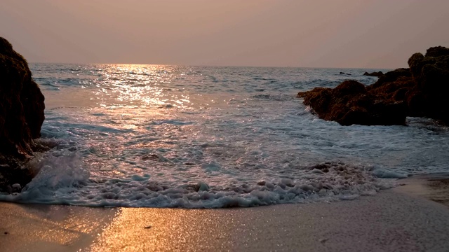 太阳反射在海面上，海浪拍打着海岸的岩石视频素材