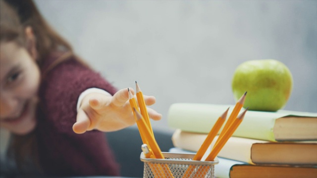 在灰色背景上接近女学生。在这段时间里，他坐在桌子旁，不能拿铅笔。视频素材