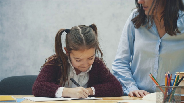 年轻的老师帮助孩子上课写字或母女学习写字，母亲教小女孩作业孤立在白色的背景下，教育学习家庭学校母亲节的概念视频素材