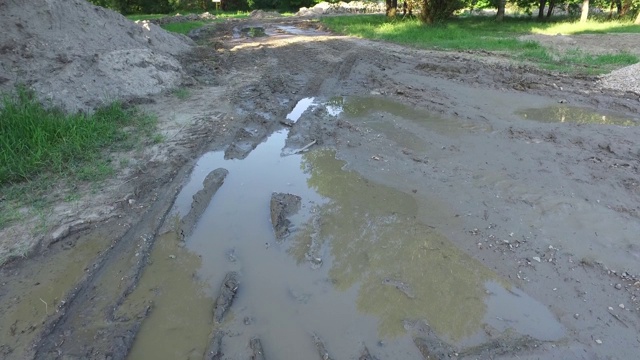 泥泞的道路上的泥坑被重型机械破坏了，留下了水坑，从上面看，地面很滑，向前移动视频素材