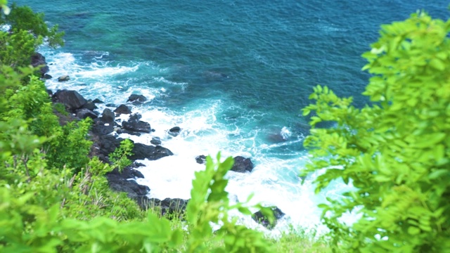 海浪拍打着岩石海滩在绿色植物的背景。暴风雨时，汹涌的海浪拍打着带有泡沫和浪花的岩石峭壁。绿松石水蚂蚁岩石悬崖景观视频素材