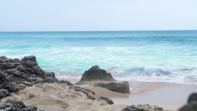 海浪拍打着沙滩景观。蓝绿色的海洋在天际线景观。沙滩上的岩石视频素材