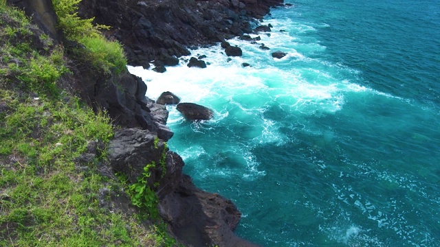 在绿色植物的背景下，海浪拍打着岩石峭壁。暴风雨时，汹涌的海浪带着泡沫和浪花溅向岩石岛。绿松石般的水压在悬崖上视频素材