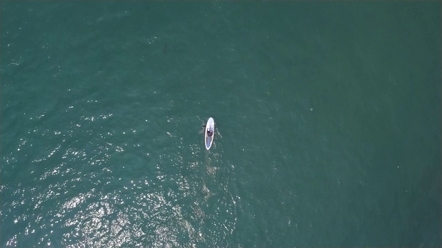 在暑假的海浪上，男人骑着立式桨板。鸟瞰图。运动员在蓝色的海洋中用桨在SUP板冲浪。水的运动。极限运动。夏天的活动视频素材