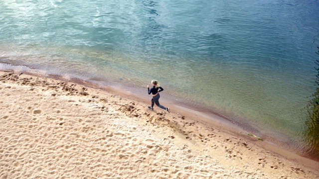 高角度锁定拍摄的年轻女性慢跑者在海滩上沿着海岸线向左的慢镜头视频素材