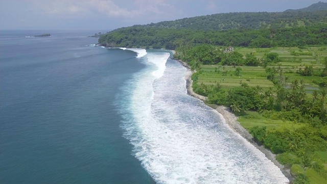 鸟瞰图蓝色的海浪和绿色的热带岛屿景观。无人机观看蓝色的海浪和稻田。印尼巴厘岛视频素材