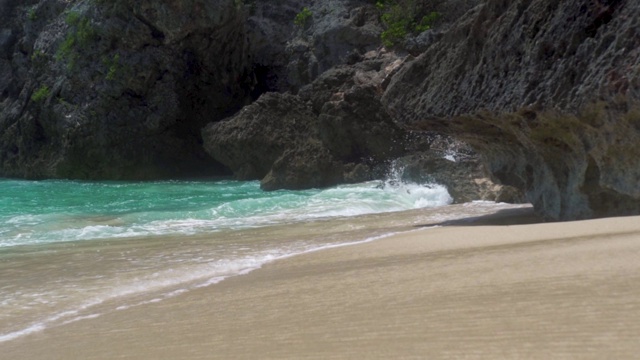 清澈的海浪拍打在沙滩上的悬崖背景。悬崖岛上碧绿的海水。热带海滩上蓝色的海浪视频素材