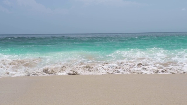 海浪碧绿的水在沙滩上蓝色的天际线景观。在地平线背景上，海浪拍打着沙滩。海的背景视频素材