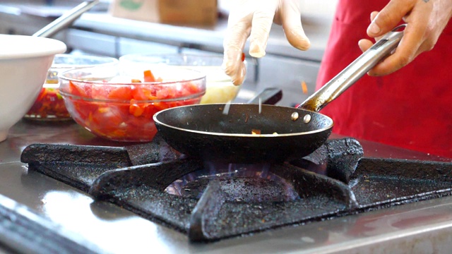 不知名的厨师在现代餐厅的厨房里烹饪素食菜肴。专业厨师在煤气炉上将食材倒入热锅中。膳食准备的概念。侧视慢动作特写视频素材