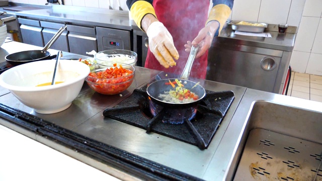 不知名的厨师在现代餐厅厨房烹制美味的素食菜肴。专业厨师将食材倒入热气腾腾的平底锅中。烹饪过程的观点。慢动作视频素材