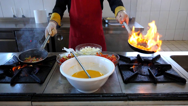 不知名的厨师拿着两个平底锅，在餐厅的现代厨房里烹饪火焰风格的菜。男厨师在炉子上的煎锅里翻炒和煎蔬菜。烹饪的概念。前视图Slowmo视频素材