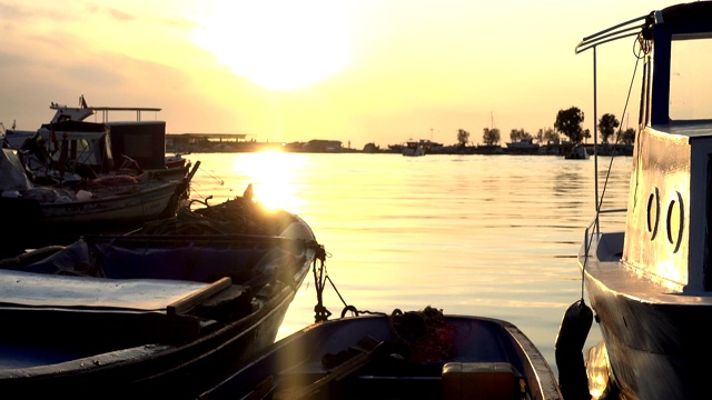 太阳开始在地平线上落下时，旧的木制渔船停泊在码头上。视频素材