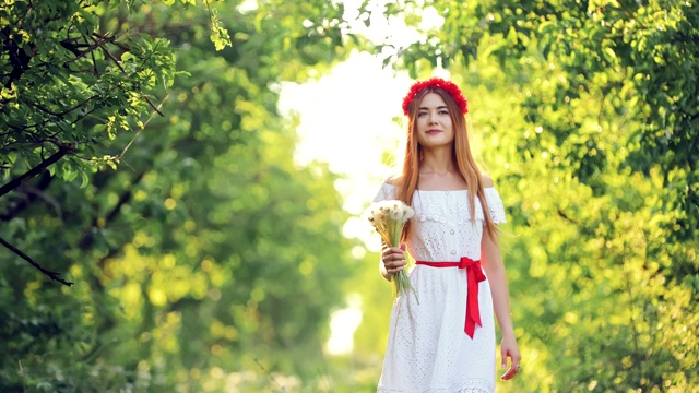 夏天，美丽的女人手里拿着一束花穿过公园。有魅力的女孩是快乐的。视频素材