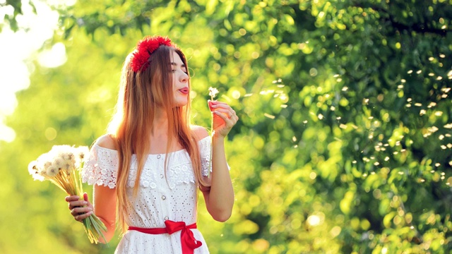 快乐的女孩穿着白色的裙子配着一束鲜花。美女吹蒲公英，花儿飞。肖像的观点。视频素材