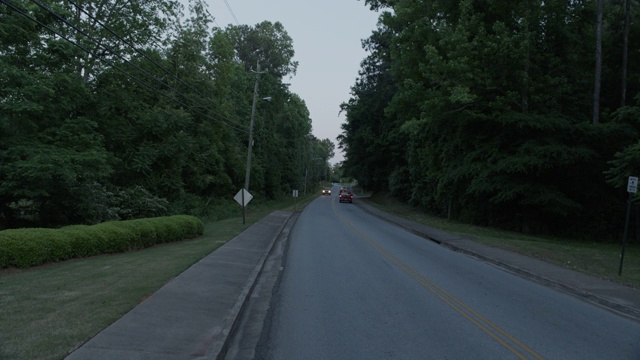 加工板直背农村，居民区或乡村道路两旁有树木。相机停止。可能是红绿灯或停车标志。人行道上可见。视频素材