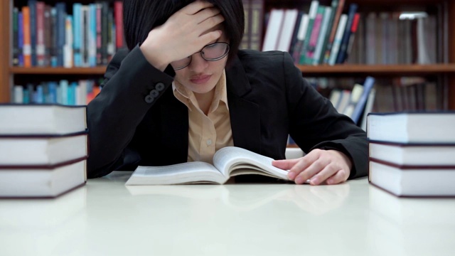 紧张的亚洲女学生戴眼镜在大学图书馆看书视频下载