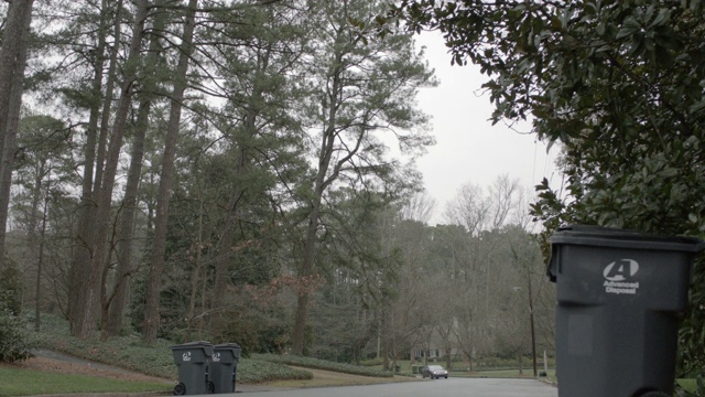 当汽车穿过上层住宅区时，从右向左。街上随处可见的垃圾桶。树线附近。可能是农村地区。在山顶可以看到大厦。视频素材