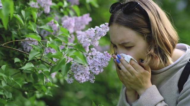 女孩有过敏喷嚏和清洁鼻子在公园附近盛开的鲜花在春天视频素材