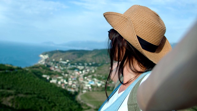 近距离微笑的旅行女人戴着太阳镜和帽子自拍显示海景享受假期视频素材