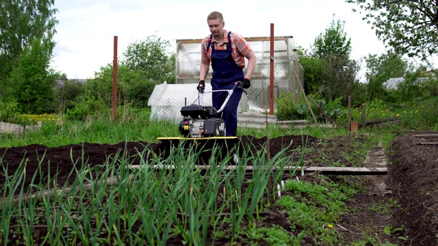 年轻的金发肌肉发达的农民用微型旋耕机耕作地面土壤。视频素材