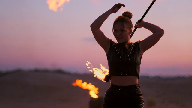 日落时，在沙滩上，手持火种的女子在美丽的天空的映衬下，慢动作地舞蹈表演。视频素材