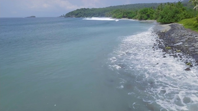 鸟瞰图蓝色的海浪和绿色的热带岛屿景观。无人机观看蓝色海浪溅在岩石海岸线上的绿色岛屿。印尼巴厘岛视频素材