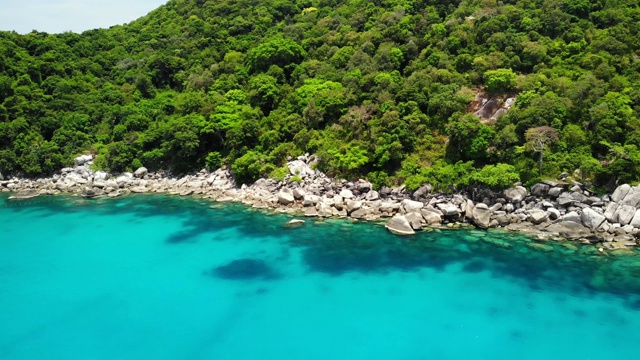 热带火山岛附近海面平静。在泰国阳光明媚的日子里，无人机在石岸附近的蓝色海洋和火山岛的绿色丛林宁静的水。视频素材