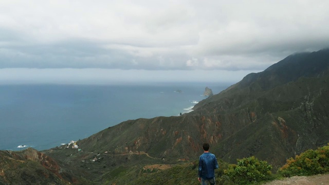 鸟瞰图。一个人站在山的边缘，看着美丽的风景——大西洋的漫长海岸，绿色的山谷和特内里费阿纳加国家公园的群山视频素材