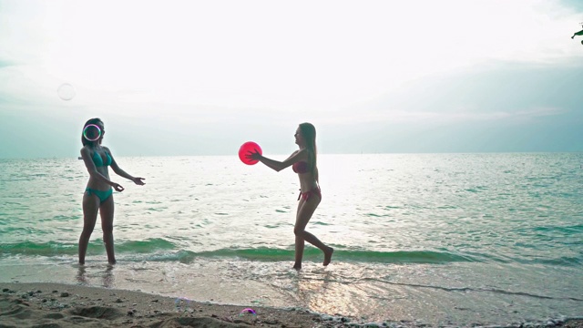 两个穿着比基尼的女孩在海边的沙滩上玩球。视频素材