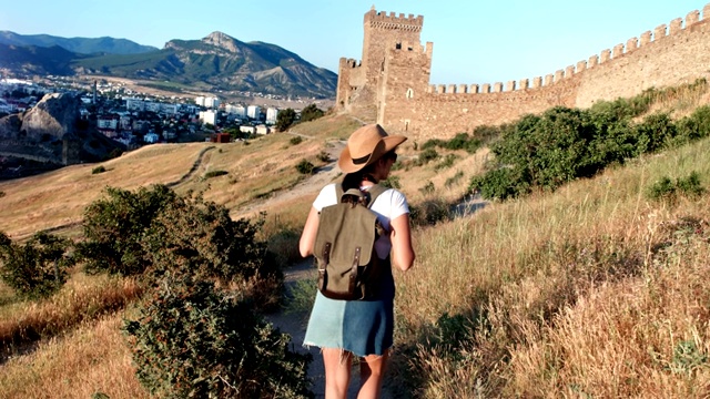 活跃的旅行背包女行走在中世纪古董墙附近的丘陵地形视频素材