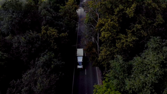 天线。白天在乡村道路上行驶的电动汽车的电影鸟瞰图。鸟瞰图飞过双车道森林道路与汽车移动绿树。汽车沿着森林道路行驶。4 k UHD视频素材