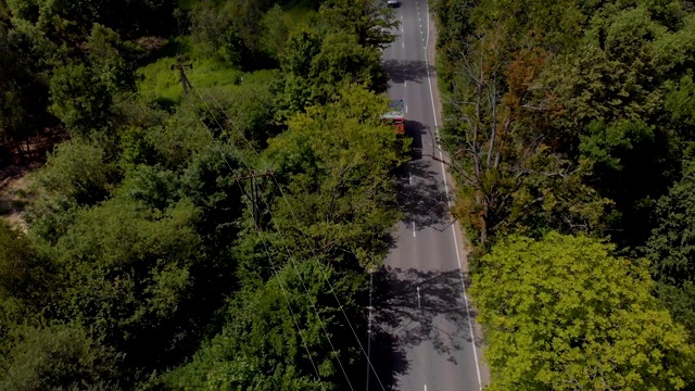 天线。白天在乡村道路上行驶的电动汽车的电影鸟瞰图。鸟瞰图飞过双车道森林道路与汽车移动绿树。汽车沿着森林道路行驶。4 k UHD视频素材