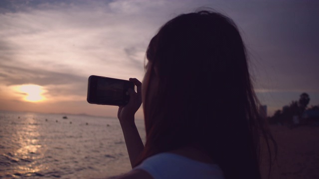 年轻女子在海滩上拍摄日落照片视频素材