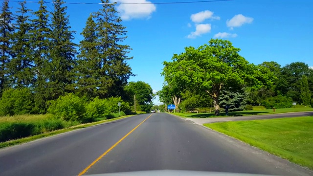 在明亮的夏日沿着民居的乡村道路行驶。司机视角:乡村街道两侧美丽的郊区房屋。视频素材