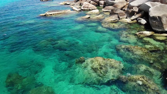 石头附近有平静的海水。在泰国阳光明媚的日子里，宁静的蓝色海水和灰色的巨石是潜水的完美场所。自然背景纹理。视频素材