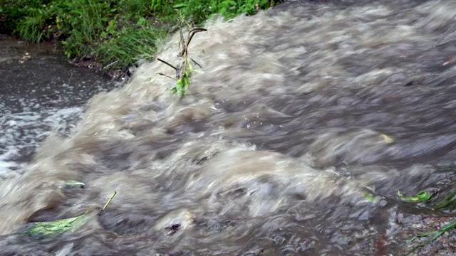 雨后肮脏、浑浊的河水在石头上流淌，然后流入河里。关闭了。4 k。视频素材