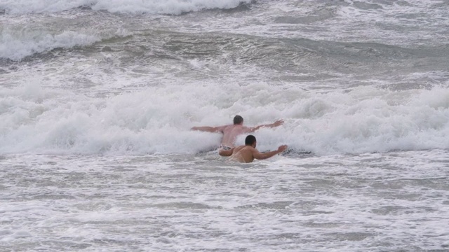 快乐的人们在暴风雨中戏水。大风时人们在海里洗澡。人们在大浪中游泳。雄企鹅在暴风雨中的波浪中跳跃。视频素材