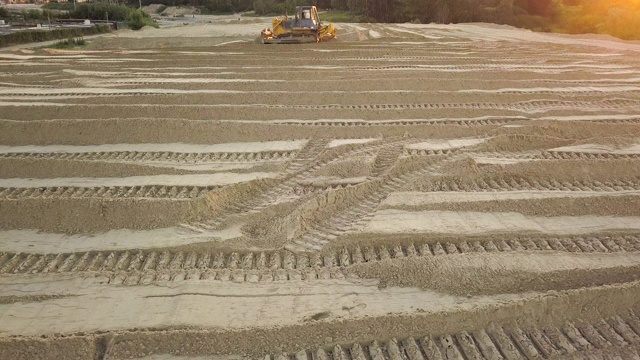 推土机的痕迹。关闭了。施工现场在道路施工现场。夏季傍晚日落时，推土机将沙子和泥土铲开。鸟瞰图视频素材