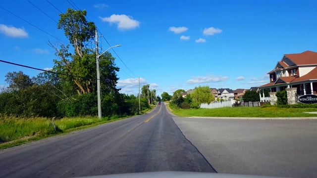 夏季驾驶绿树成荫的住宅城市道路。司机视角沿着美丽的阳光郊区街道。视频素材