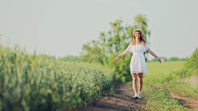 美丽的女孩穿着白色的衣服，戴着帽子走在一条乡间小路上。国家风景。视频素材