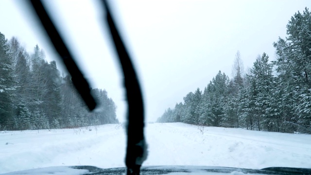 一辆汽车在大雪中沿着一条覆盖着积雪的森林道路行驶。视频素材