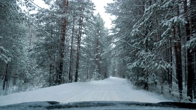 一辆汽车在大雪中沿着一条覆盖着积雪的森林道路行驶。视频素材