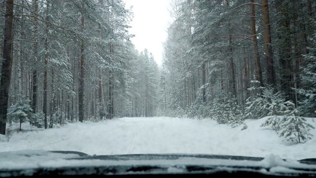 一辆汽车在大雪中沿着一条覆盖着积雪的森林道路行驶。视频素材